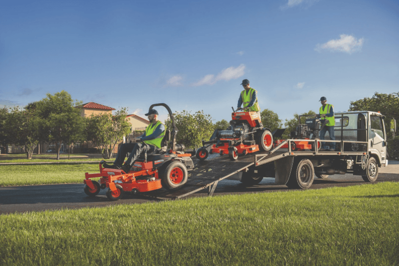 Landscapers driving mowers off the back of a trailer