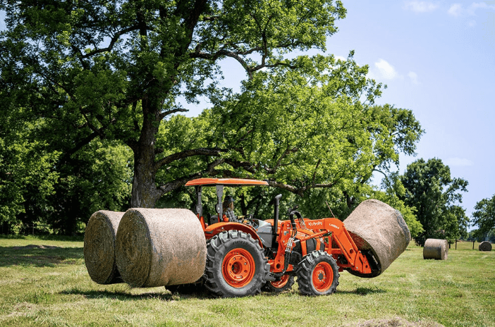 Kubota M5 Series tractor moving hay bales with rear and front attachments