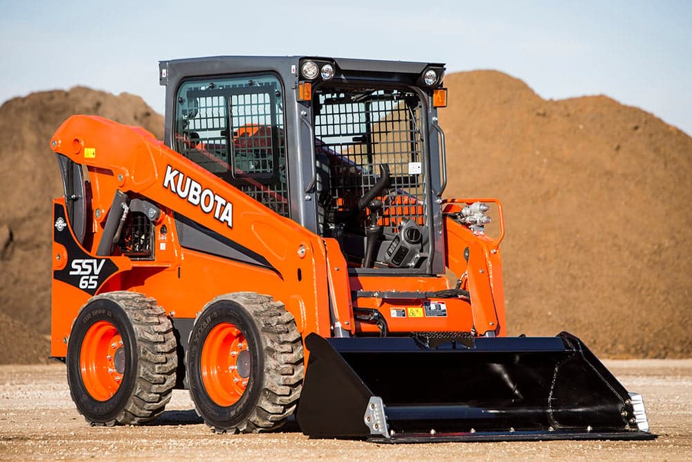 Kubota SSV65 skid steer loader with bucket attachment in front of dirt piles