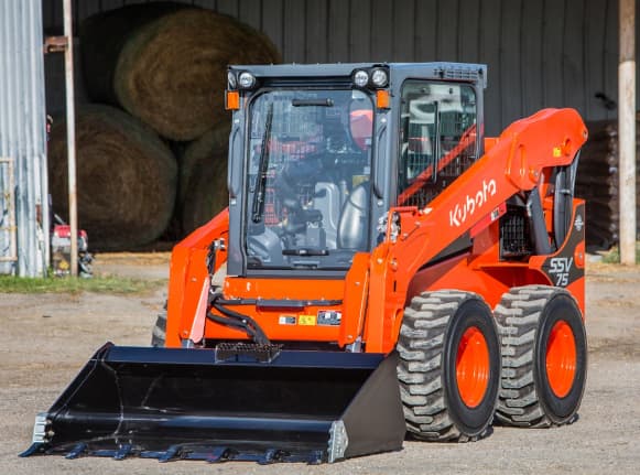Kubota SSV75 skid steer loader with bucket attachment parked in a barn